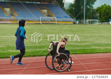 A Muslim woman in a burqa running together with a woman in a wheelchair on the marathon course, preparing for future competitions. 127568695