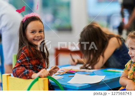 Creative kids during an art class in a daycare center or elementary school classroom drawing with female teacher. Creative kids during an art class in a daycare center or elementary school classroom drawing with female teacher. 127568743