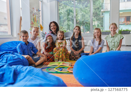 A happy female teacher sitting and playing hand games with a group of little schoolchildren 127568775