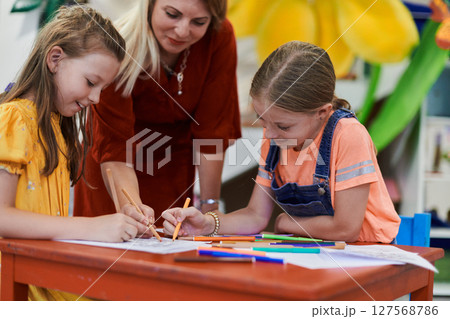 Creative kids during an art class in a daycare center or elementary school classroom drawing with female teacher. 127568786