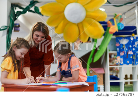 Creative kids during an art class in a daycare center or elementary school classroom drawing with female teacher. Creative kids during an art class in a daycare center or elementary school classroom drawing with female teacher. 127568787