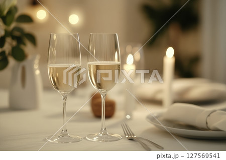 Romantic dinner setting with two champagne glasses on elegant white tablecloth. Soft candlelight in background. Blurred cozy ambiance. Elegant and intimate mood. Fine dining concept. Copy space Romantic dinner setting with two champagne glasses on elegant white tablecloth. Soft candlelight in background. Blurred cozy ambiance. Elegant and intimate mood. Fine dining concept. Copy space 127569541