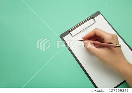 A female hand hold a pen and black clipboard with paper on mint background. 127569821