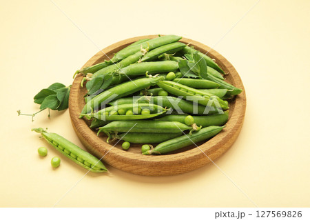 Fresh green peas in wooden bowl with pods and leaves on beige background, healthy green vegetable or legume 127569826