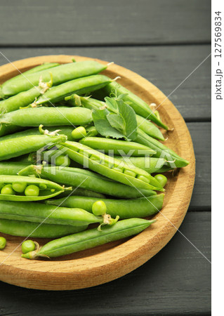 Fresh green peas in wooden bowl with pods and leaves on black wooden background. Vertical photo 127569834