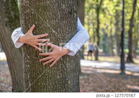 Close up of protective child hands embracing tree trunk in summer park. Care about nature concept. 127570567