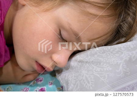 Close up of a face of pretty little child girl with slightly open mouth and scattered around hair sleeping in bed at home. 127570573