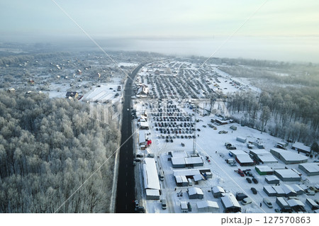 Aerial view of winter landscape with snow covered woods and black asphalt forest road on cold wintry day 127570863