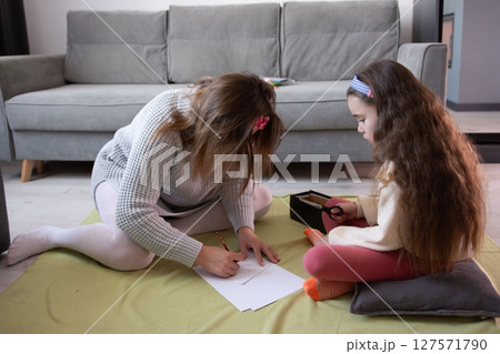 A mother and daughter spend quality time together, engaging in a creative activity at home. They are drawing and cutting, fostering a loving bond. 127571790