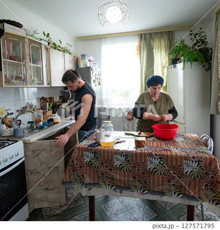 Cooking together in a cozy kitchen as a young man helps an elderly woman prepare a delicious meal while sharing stories and laughter 127571795