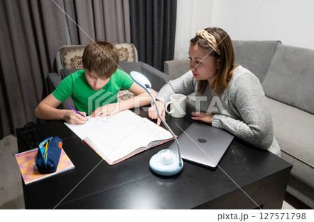 On a cozy evening at home, a child is deeply engaged in a focused study session while a parent provides supportive guidance, creating a warm learning atmosphere On a cozy evening at home, a child is deeply engaged in a focused study session while a parent provides supportive guidance, creating a warm learning atmosphere 127571798