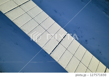 Aerial view of snow covered sustainable electric power plant with rows of solar photovoltaic panels for producing clean electrical energy. Low effectivity of renewable electricity in northern winter Aerial view of snow covered sustainable electric power plant with rows of solar photovoltaic panels for producing clean electrical energy. Low effectivity of renewable electricity in northern winter 127571830