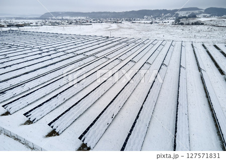 Aerial view of snow covered sustainable electric power plant with rows of solar photovoltaic panels for producing clean electrical energy. Low effectivity of renewable electricity in northern winter Aerial view of snow covered sustainable electric power plant with rows of solar photovoltaic panels for producing clean electrical energy. Low effectivity of renewable electricity in northern winter 127571831
