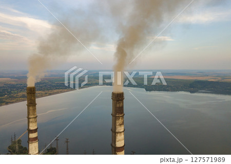 Aerial view of high chimney pipes with grey smoke from coal power plant. Production of electricity with fossil fuel. Aerial view of high chimney pipes with grey smoke from coal power plant. Production of electricity with fossil fuel. 127571989
