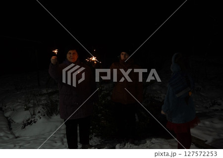 Three generations light sparklers on a snowy night, celebrating the new year with joy and warmth. Three generations light sparklers on a snowy night, celebrating the new year with joy and warmth. 127572253