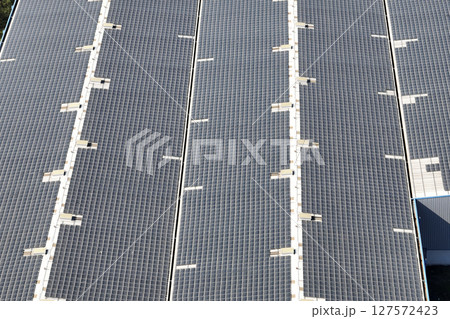 Aerial view of blue photovoltaic solar panels mounted on industrial building roof for producing green ecological electricity. Production of sustainable energy concept Aerial view of blue photovoltaic solar panels mounted on industrial building roof for producing green ecological electricity. Production of sustainable energy concept 127572423