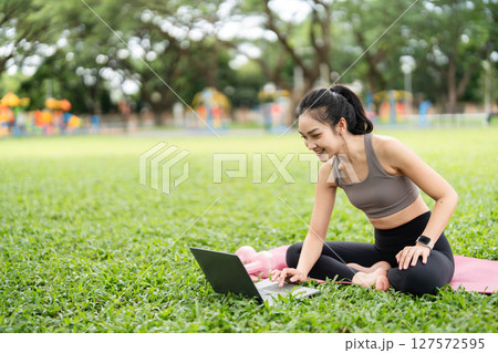 Yoga and Digital Wellness. Smiling woman using laptop while practicing yoga outdoors. Yoga and Digital Wellness. Smiling woman using laptop while practicing yoga outdoors. 127572595