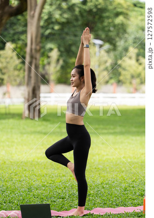 Yoga and balance. Young woman practicing tree pose outdoors in a green park. 127572598