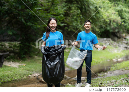 Joyful volunteers. Young couple smiling while cleaning nature. Joyful volunteers. Young couple smiling while cleaning nature. 127572600
