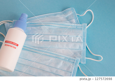 Desinfection spray and medical mask for hygiene on the blue background with place for text. Antibacterial, against pollution or virus protection. Desinfection spray and medical mask for hygiene on the blue background with place for text. Antibacterial, against pollution or virus protection. 127572698