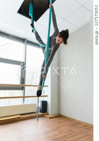 Woman performing aerial silks acrobatics in bright dance studio. Woman performing aerial silks acrobatics in bright dance studio. 127573051
