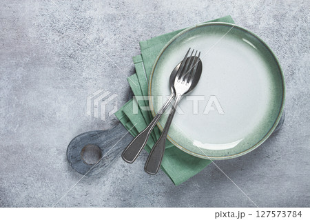 an empty plate and cutlery laid out, on a cutting board, with a green napkin, a gray table, top view, an empty plate and cutlery laid out, on a cutting board, with a green napkin, a gray table, top view, 127573784