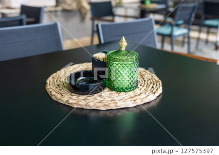 Green glass jar and sugar packets on woven placemat. Cafe table setting, casual dining ambiance and stylish hospitality decor. 127575397