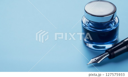 A blue ink bottle and a fountain pen placed neatly on a blue surface 127575933