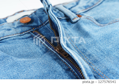 Close-up of denim jeans button and zipper, detailed view of textile, stitching, and copper hardware Close-up of denim jeans button and zipper, detailed view of textile, stitching, and copper hardware 127576541