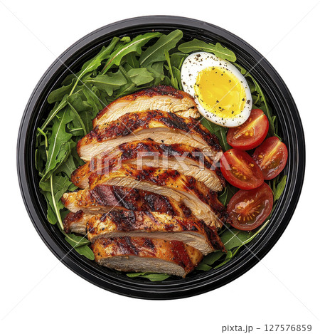 Grilled chicken salad with arugula, cherry tomatoes, and boiled egg on dark plate, seasoned with pepper. dish is vibrant and appetizing, perfect for healthy meal 127576859