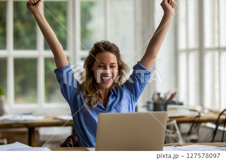 自宅ワークスペースで自己の成功を祝うエネルギッシュな若い女性 127578097
