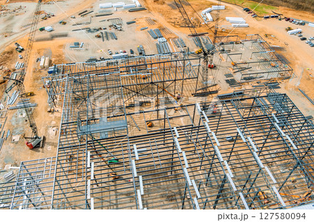 Workers are assembling large steel framework at busy construction site surrounded by materials. Workers are assembling large steel framework at busy construction site surrounded by materials. 127580094