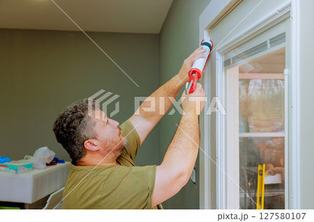 Man works diligently to caulk window frame in home renovation project, his handyman skills. 127580107