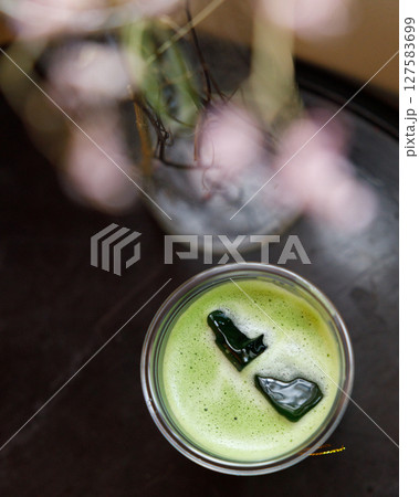 Top view of Cup of fresh matcha tea, green tea on wooden table with flower as foreground. 127583699
