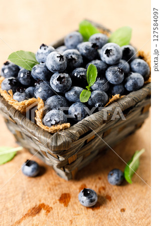 Ripe blueberries in wicker basket on wooden table. 127584097
