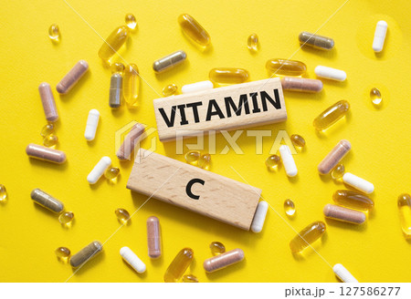 Vitamin C symbol. Concept word Vitamin C on wooden blocks. Beautiful yellow background with pills. Medicine and Vitamin C concept. Copy space Vitamin C symbol. Concept word Vitamin C on wooden blocks. Beautiful yellow background with pills. Medicine and Vitamin C concept. Copy space 127586277