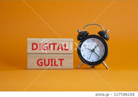Digital Guilt symbol. Concept words Digital Guilt on wooden blocks. Beautiful orange background with alarm clock. Business and Digital Guilt concept. Copy space. 127586288