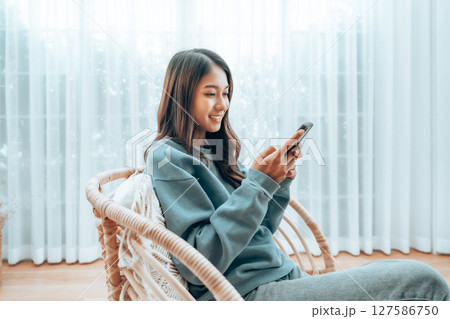 Young Asian Woman Relaxing in Modern Wicker Chair Near Window with Sheer Curtain Young Asian Woman Relaxing in Modern Wicker Chair Near Window with Sheer Curtain 127586750