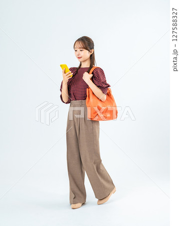 スマホを持って歩くカジュアルウェアの女性の全身写真 127588327