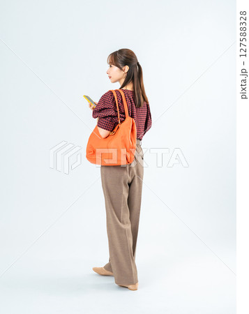 スマホを持って歩くカジュアルウェアの女性の全身写真 127588328