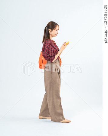 スマホを持って歩くカジュアルウェアの女性の全身写真 127588329