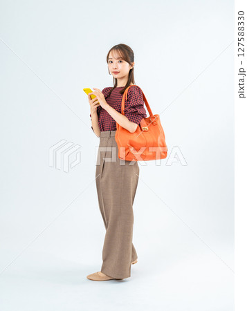 スマホを持って歩くカジュアルウェアの女性の全身写真 127588330