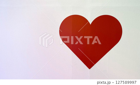 A bold red heart symbol painted on a clean white wall. Minimalist design representing love, care, or emotional connection. 127589997