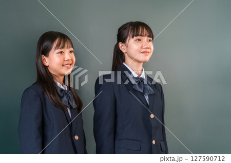 教室の黒板の前に立つ制服姿の友達,小学生,中学生,高校生の女子生徒 127590712