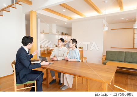 リビングで商談するビジネスマンと若い夫婦 リビングで商談するビジネスマンと若い夫婦 127590999