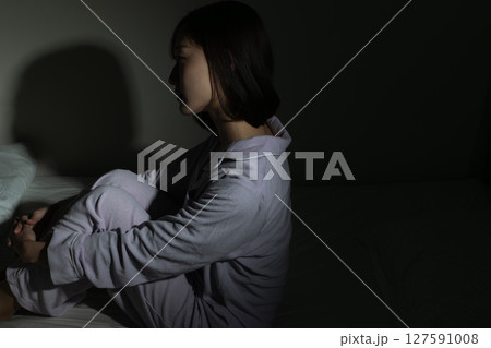 暗闇の中でベッドに座り悩んでいる若い女性 127591008