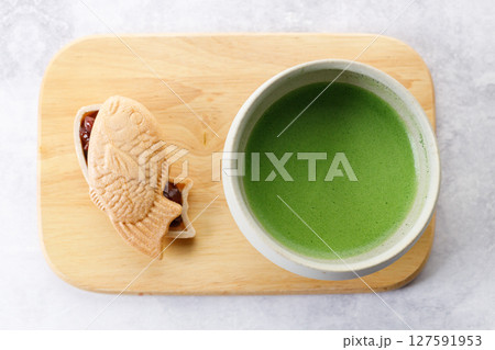 Cup of fresh matcha tea, green tea and Taiyaki, Japanese fish-shaped cake, filled with Anko or red bean on wooden plate. Cup of fresh matcha tea, green tea and Taiyaki, Japanese fish-shaped cake, filled with Anko or red bean on wooden plate. 127591953