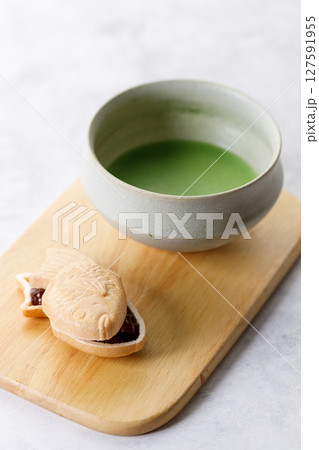 Cup of fresh matcha tea, green tea and Taiyaki, Japanese fish-shaped cake, filled with Anko or red bean on wooden plate. 127591955