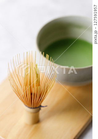 Cup of fresh matcha tea, green tea and Chasen, bamboo whisk, on wooden plate on white table. Cup of fresh matcha tea, green tea and Chasen, bamboo whisk, on wooden plate on white table. 127591957