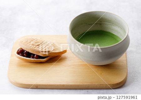 Cup of fresh matcha tea, green tea and Taiyaki, Japanese fish-shaped cake, filled with Anko or red bean on wooden plate. 127591961